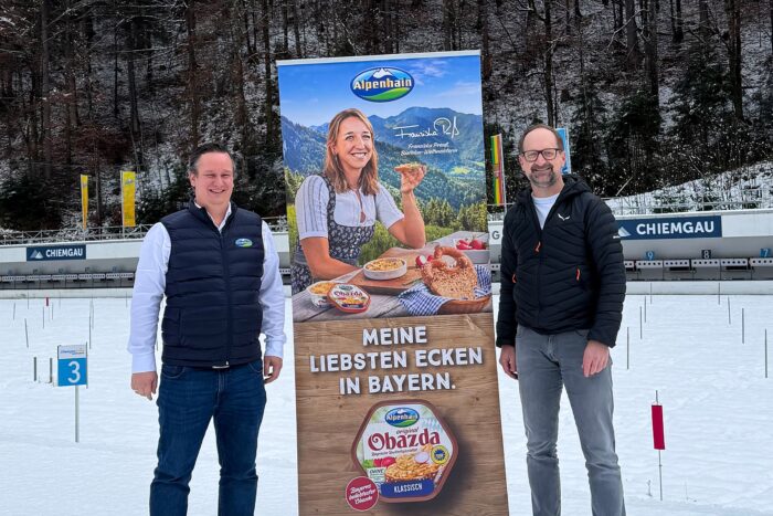 Alpenhain-wird-offizieller-Partner_Titelbild Vertreter von Alpenhain und der Chiemgau Arena vor Werbedisplay im Stadionbereich in Ruhpolding.