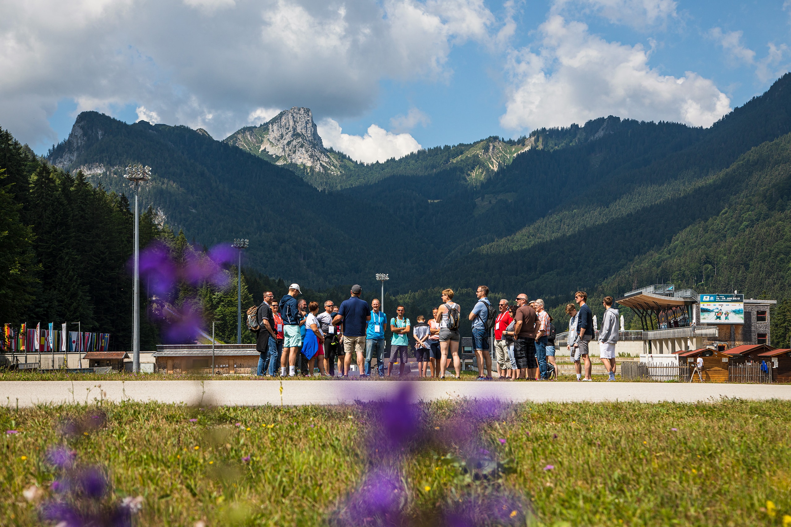 Arena-Tour mit Besuchergruppe auf dem Gelände der Chiemgau Arena vor Bergkulisse in Ruhpolding.