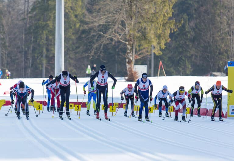 Startszene eines Langlaufrennens mit mehreren Athleten auf der präparierten Loipe.