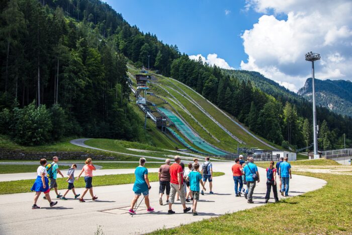 arena-touren_IU2A4183 Gruppe bei geführtem Rundgang durch das Stadiongelände der Chiemgau Arena vor Skisprungschanzen.