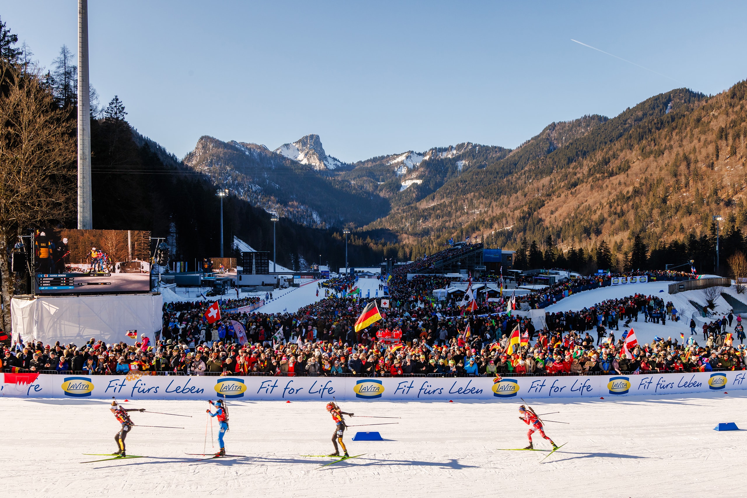 Biathlon-Wettkampf in der Chiemgau Arena mit voll besetzten Tribünen und Alpenpanorama im Hintergrund.